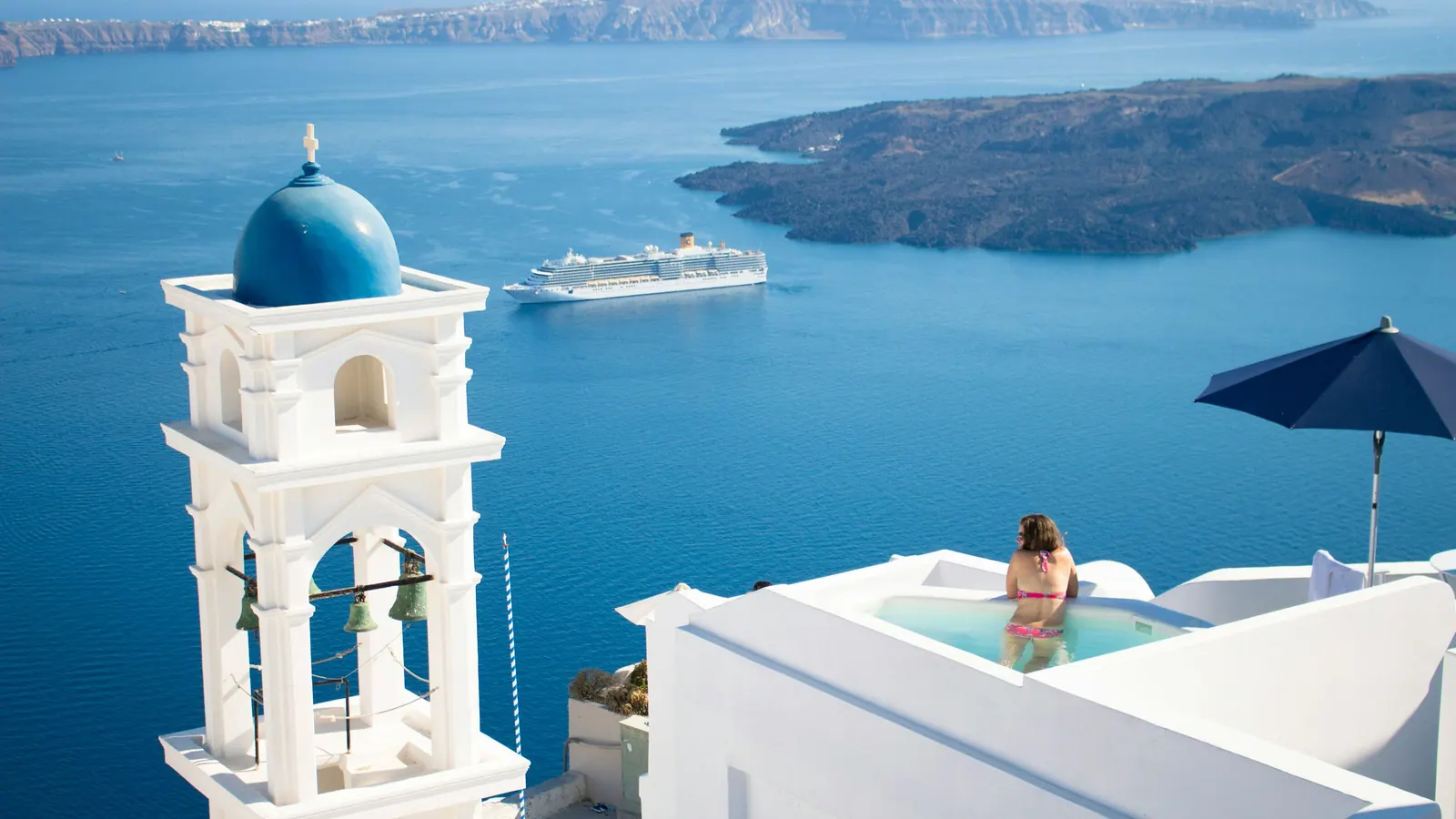 A hotel terrace in Imerovigli with its bell tower and a cruise ship anchored in the caldera