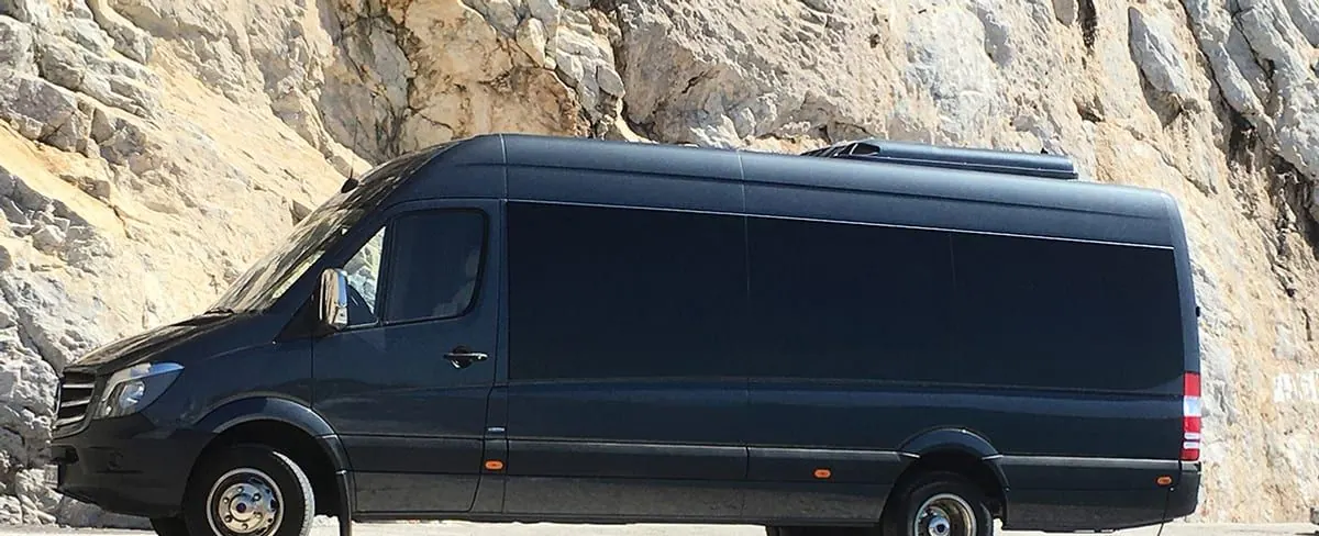 The operator's black minibus on a cliff road in Santorini